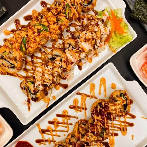 Two plates of sushi rolls with various toppings, shrimp, crab, and peppers on a dark surface.