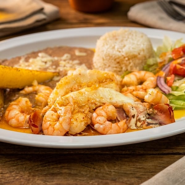 A white plate with shrimp, rice, refried beans, fried plantains, and a side salad.