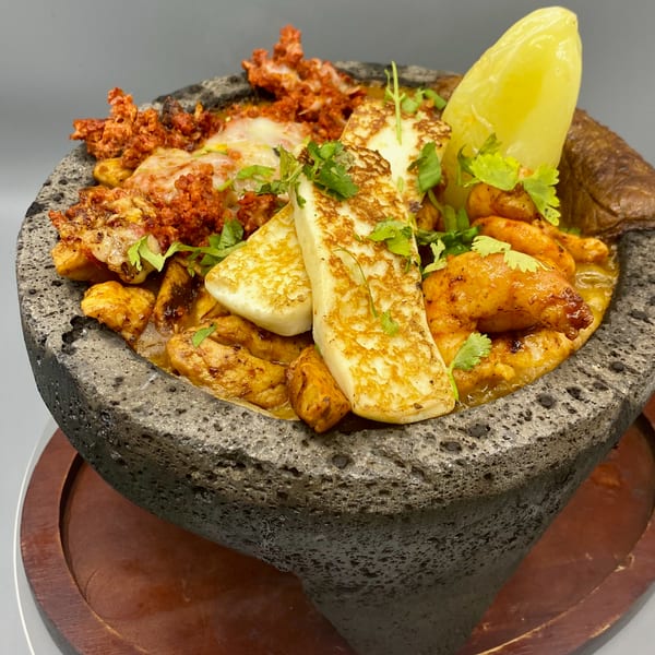 A molcajete filled with grilled chicken, chorizo, cheese, and a yellow pepper, garnished with cilantro.