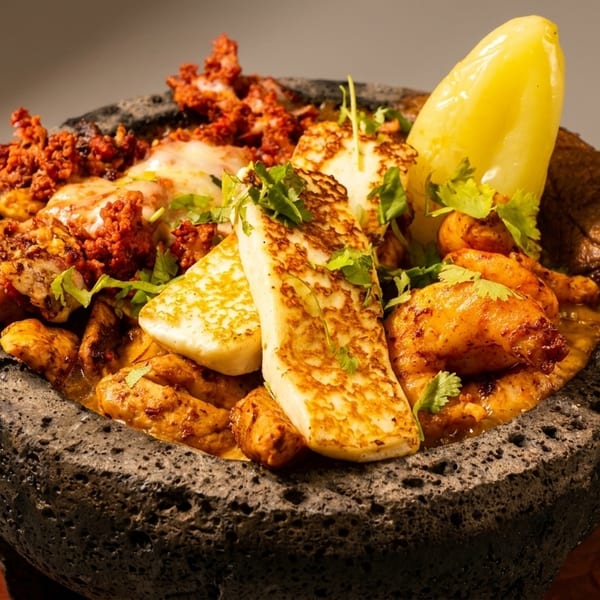 A molcajete filled with grilled chicken, chorizo, cheese, and a yellow pepper, garnished with cilantro.